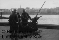 Ein 2cm-Flakgeschütz am Rheinufer. Im Hintergrund die Kölner Altstadt.
